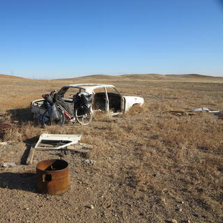 My bike leans against the back of a derelict car.