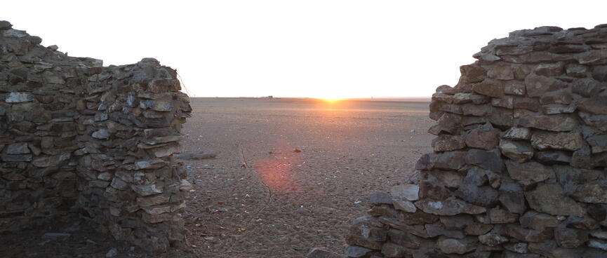 A bright sunrise viewed through a gap in the buildingʼs wall.
