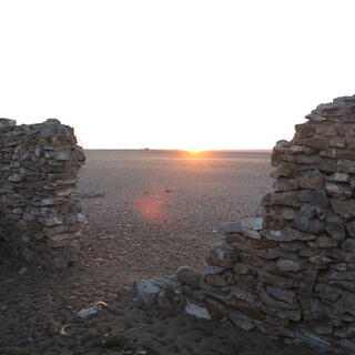 A bright sunrise viewed through a gap in the buildingʼs wall.