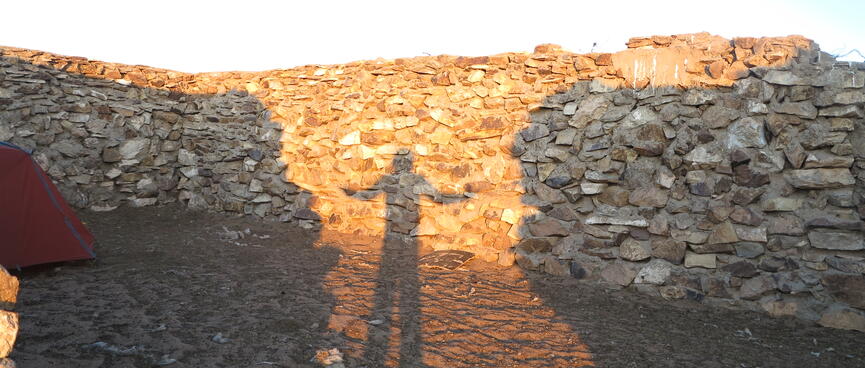 My backlit shadow stretches its arms wide between shadows of walls.