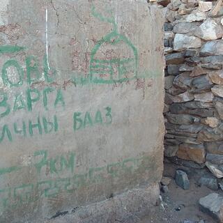 A concrete wall contains a painted message and a picture of a dome, which is presumably a ger.