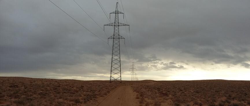 A line of power pylons next to a sandy path.