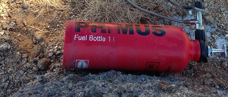 A Primus Fuel Bottle lies on its side while connected to a Primus stove.