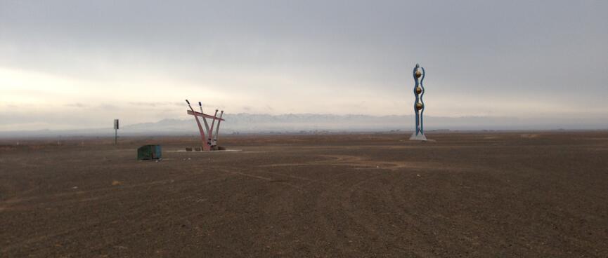 Two monuments - the one on the left is two offsets Vees, the one on the right is three vertical golden balls wrapped in wavy blue arms.