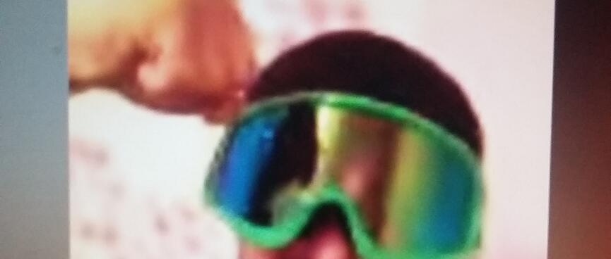 During an internet chat, a man wearing green mirrored goggles pumps his fist in the air.