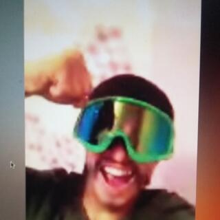 During an internet chat, a man wearing green mirrored goggles pumps his fist in the air.