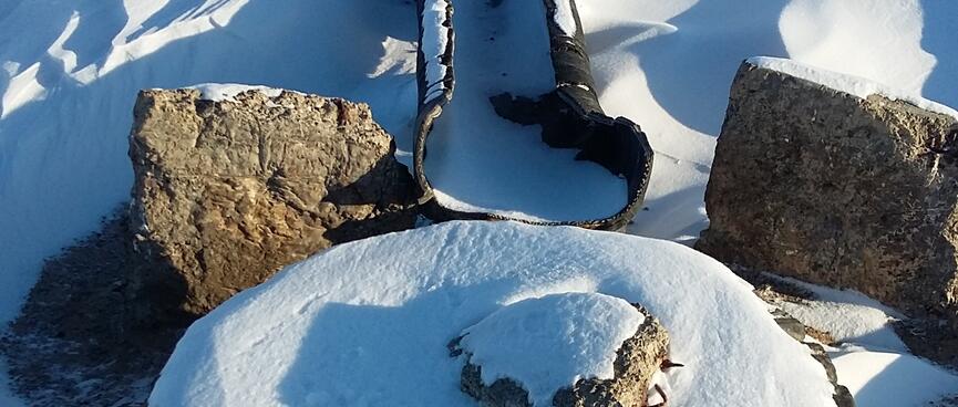 A snow covered tyre lies at the top of a rise, A metal trough sits below.