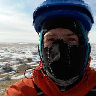 Dressed balaclava, hoodie and helmet, I pose in front of a scene of snowdrifts.
