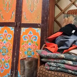 A wooden wardrobe with ornately painted panes stands next to a pair of tall boots and a comfortable sitting with a grid pattern.
