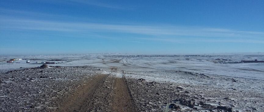 A cluster of buildings at the end of a dirt road partially covered in snow.