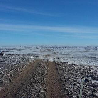 A cluster of buildings at the end of a dirt road partially covered in snow.