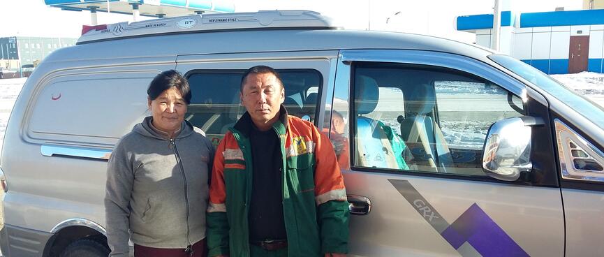 A woman in street clothes and a man in overalls stand in front of their van.