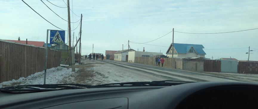Groups of people dressed in coats and hats walk down a town street.