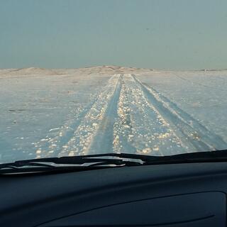View out the windscreen to tyre tracks through the snow.