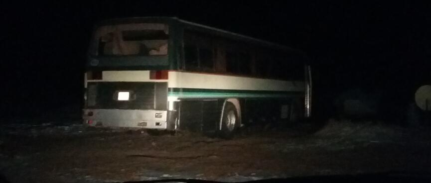The vanʼs headlights illuminate a parked bus.