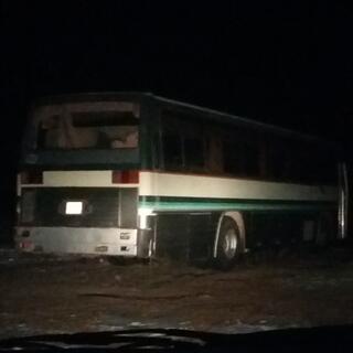 The vanʼs headlights illuminate a parked bus.