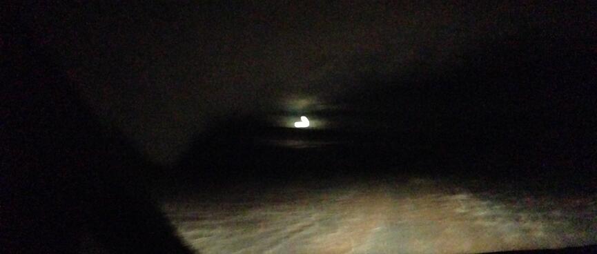 The vanʼs headlights illuminate the road, a bright light shines in the distance.