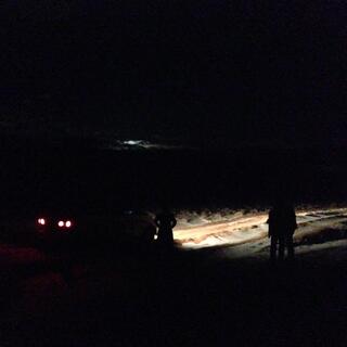 The silhouette of a person standing next to a van on a snowy dirt road.