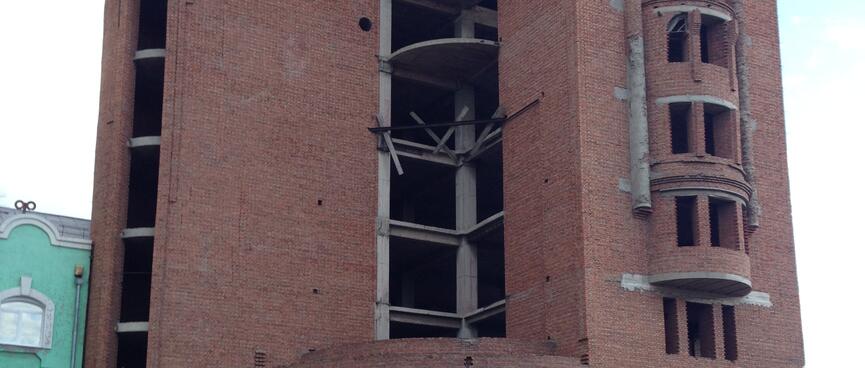 A curved six story brick is held together by scaffolding, at Zabaikalsk.