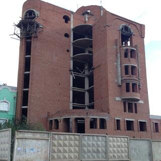 A curved six story brick is held together by scaffolding, at Zabaikalsk.