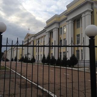 Four story yellow buildings with white rectangular columns sit behind tall metal gates, in Chita.