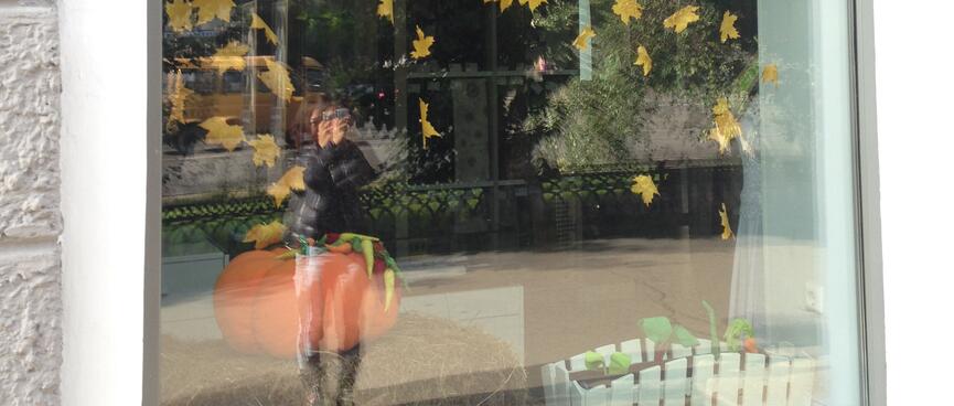 A window display of yellow leaves catches reflections of trees and Wanna with her camera, in Chita.