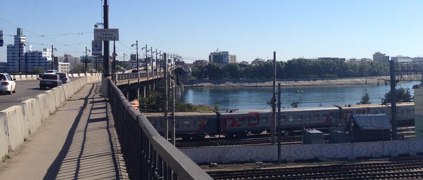 The bright sun casts shadows through the railing of a long bridge.