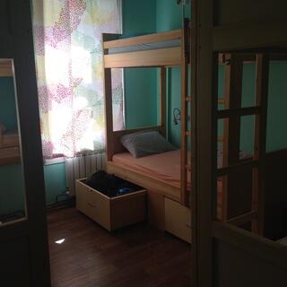 A room of bunks is partially illuminated by thin floral curtains.