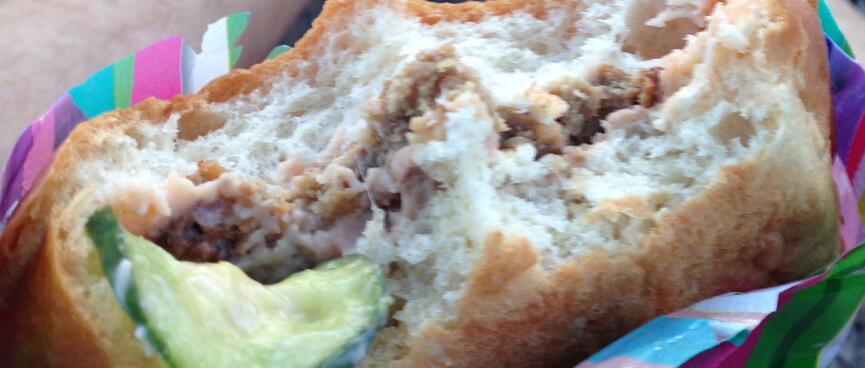 Thick bread buns, a layer of meat, and a floppy piece of cucumber.
