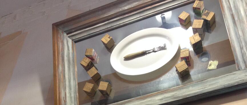 An artwork contains a dinner plate, a fork, and many small cubes.