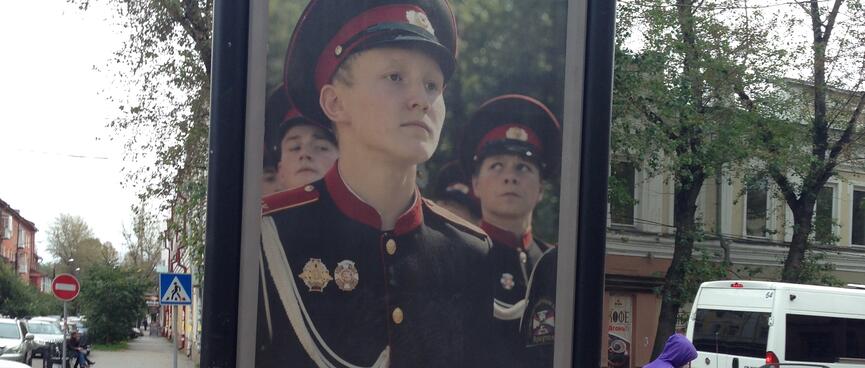 A billbaord shows three boys standing to attention while dressed in military uniform.