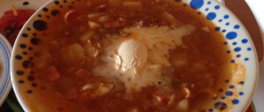 Ham and vegetables in a red broth, with a dollop of sour cream, and a slice of bread.