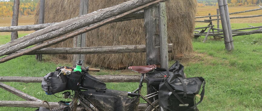 My mud-caked bike is dwarfed by a mound of grass, protected by an open-sided shed.