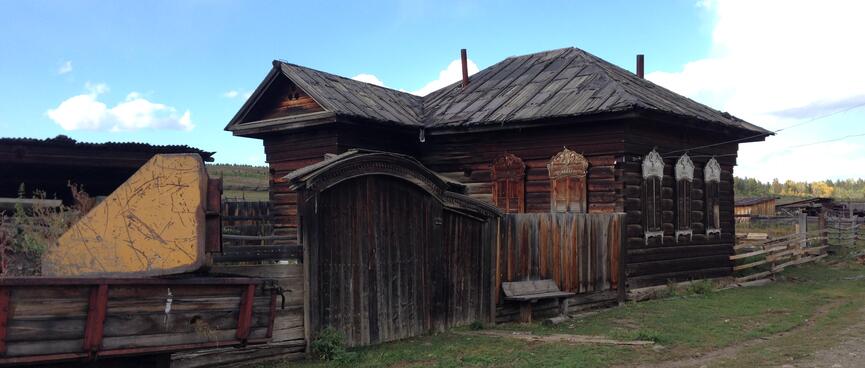 A wooden cart stands outside a wooden house with shuttered windows.