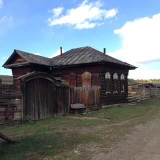 A wooden cart stands outside a wooden house with shuttered windows.