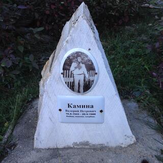 A wedge of white stone bears a plaque and a photograph of a man.