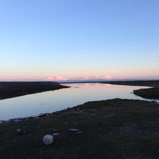 A motorcycle stands next to an inlet at sunset.