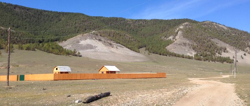 Two farm houses at the foot of tree covered hills.