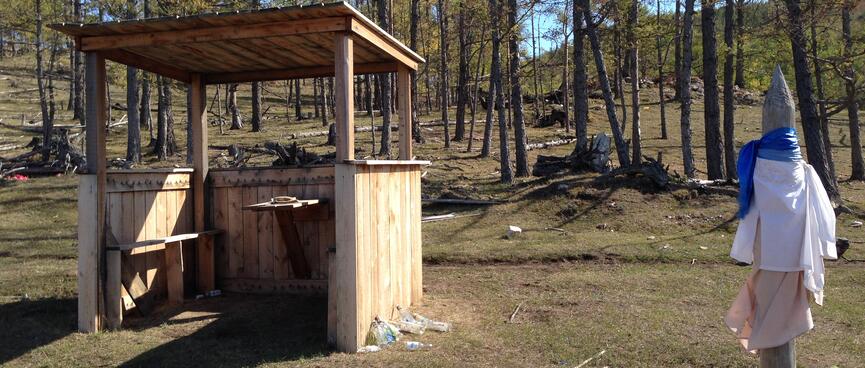 An open wooden shelter contains bench seats and a wall mounted table.