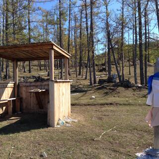 An open wooden shelter contains bench seats and a wall mounted table.