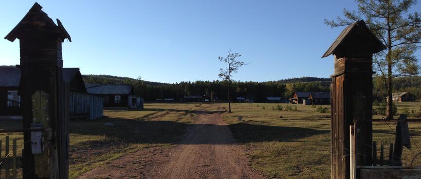 Behind wooden gate posts, a number of long single story houses are visible.