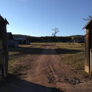 Behind wooden gate posts, a number of long single story houses are visible.