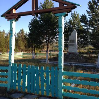 A small stone memorial sits behind an elaborate teal wooden gate.
