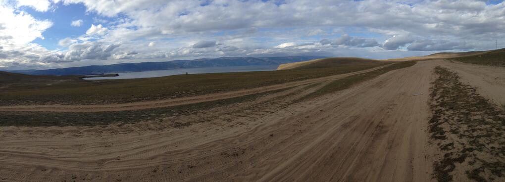 A wide dirt road is imprinted with many tyre tracks.