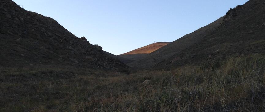 At the foot of a grassy valley, a sunlit hilltop is just visible in the distance.