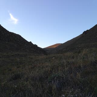 At the foot of a grassy valley, a sunlit hilltop is just visible in the distance.