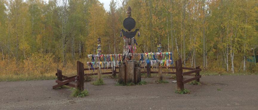 A metal disc on a pole stands in the middle of a wooden shrine.