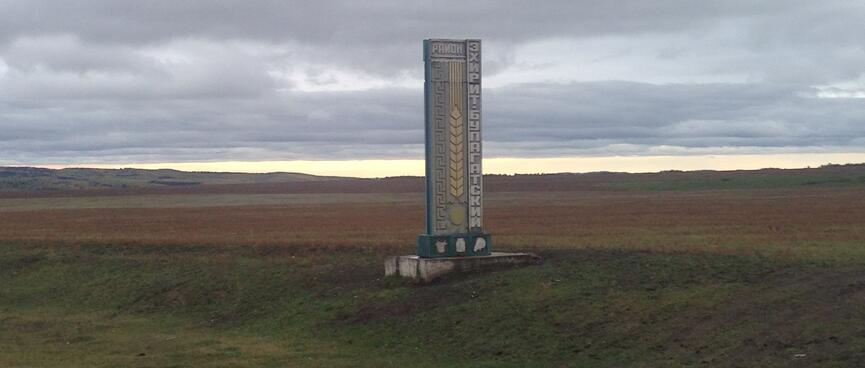 A tall stone sign in the middle of a field.