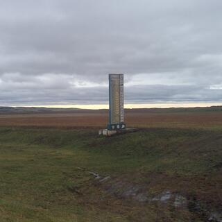 A tall stone sign in the middle of a field.