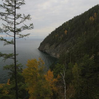 A forested hill ends in rocky walls rising from the lake.